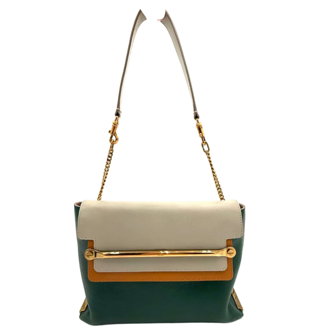 A color-blocked leather shoulder bag with a dark green base, cream top flap, and tan horizontal accent stripe, featuring gold-tone hardware and a gold chain strap, held by a hand against a bright white studio backdrop.
