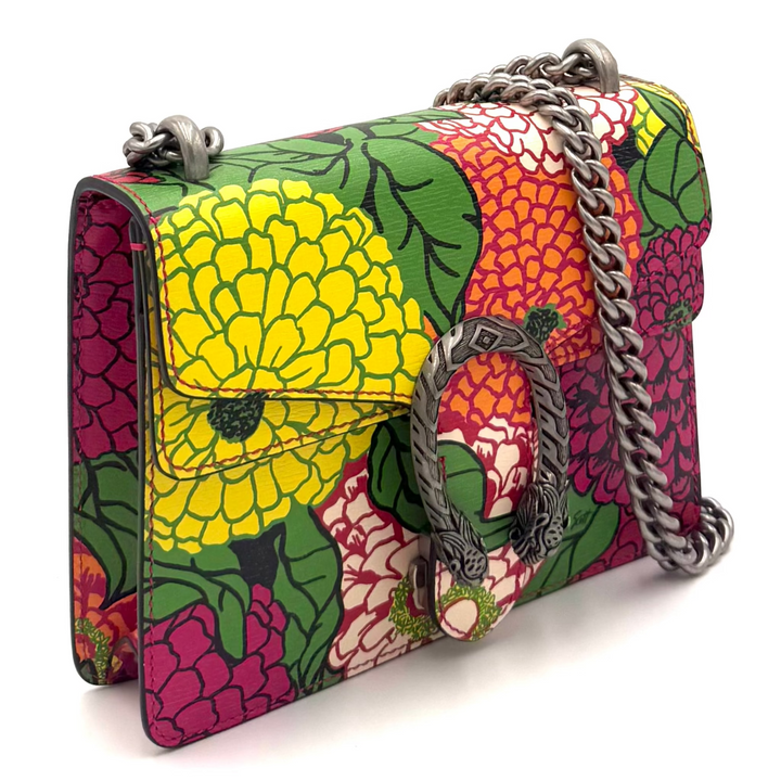 A Gucci shoulder bag featuring a vibrant fruit and floral print in yellow, pink, green, and red, with a silver-tone chain strap and the brand's horsebit logo on the front.