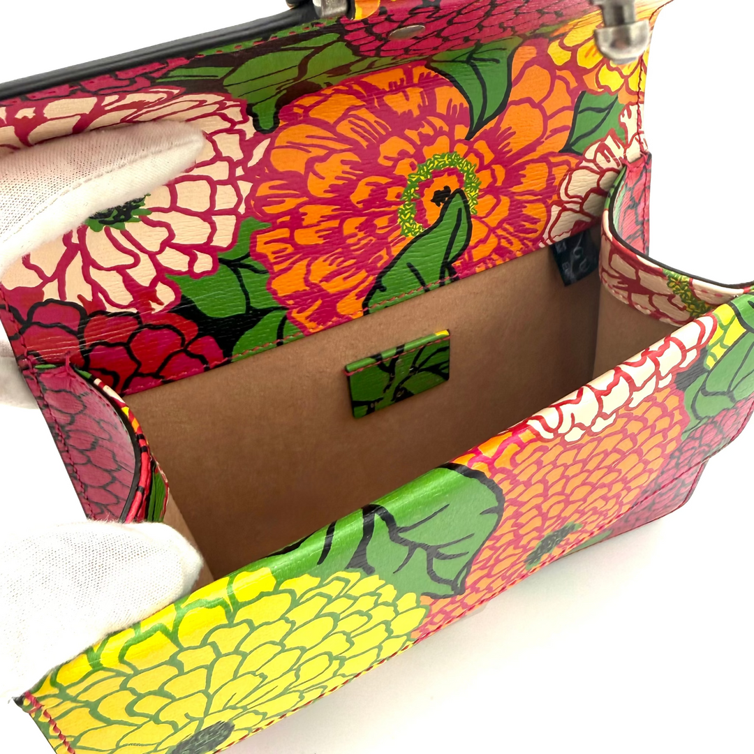 A colorful floral clutch bag with a vibrant multicolor print of orange, pink, yellow, and green flowers. It features a brown interior lining and ornate silver-tone metal clasp closures shaped like lions, shown open on a white background.