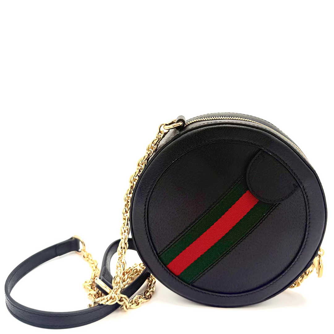 A black leather round shoulder bag featuring the signature red and green web stripe on the front, with a gold chain strap and black leather strap, set against a plain white background.