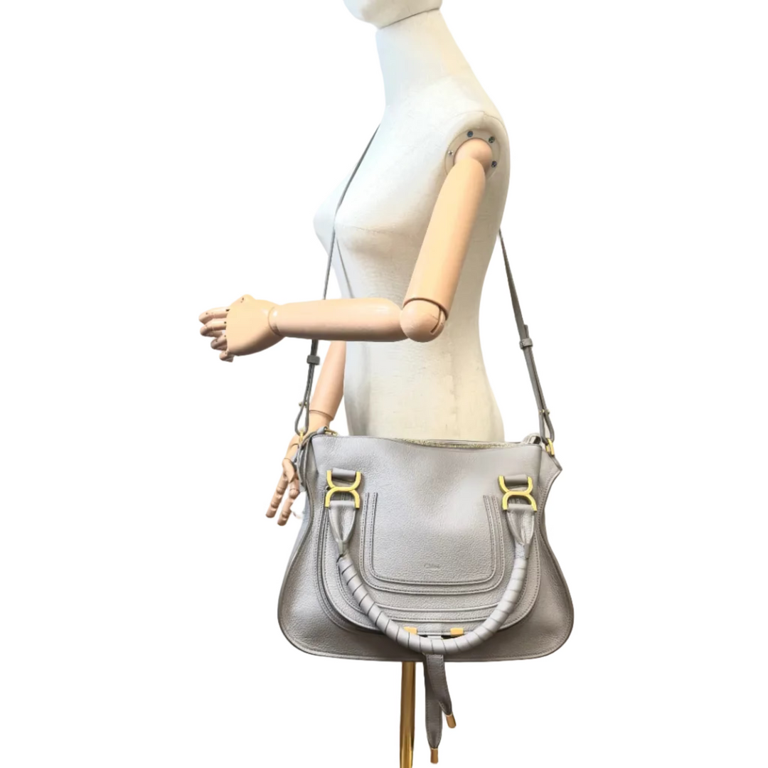 A light gray leather shoulder bag with gold-tone hardware and a gray beaded strap detail, displayed on a wooden-armed mannequin against a white background.