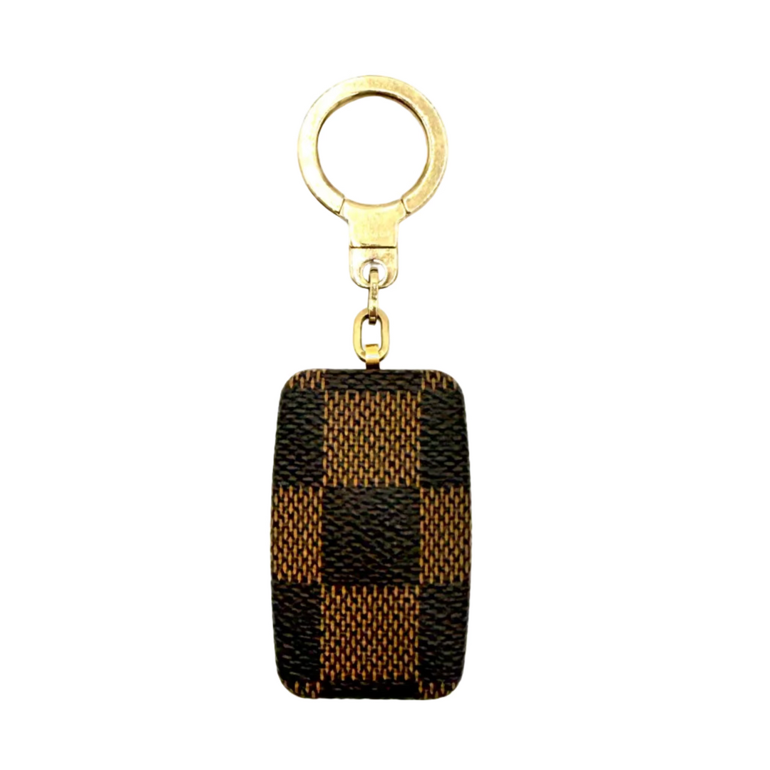 A Louis Vuitton keychain featuring a rectangular canvas charm in the brand's signature Damier check pattern, attached to a gold-tone split ring and clasp, set against a plain white background.
