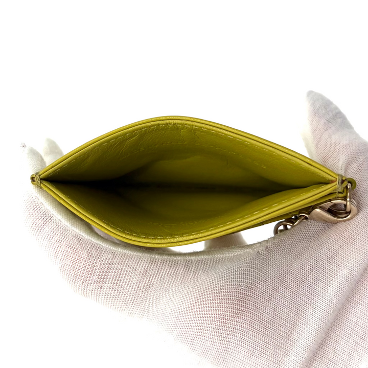 A small zippered pouch or card holder shown open, held by a white gloved hand against a plain white background.