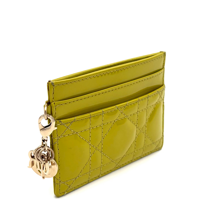 A slim, quilted card holder wallet in a vibrant olive green patent leather with gold-tone hardware and a hanging key charm, shown on a plain white background.