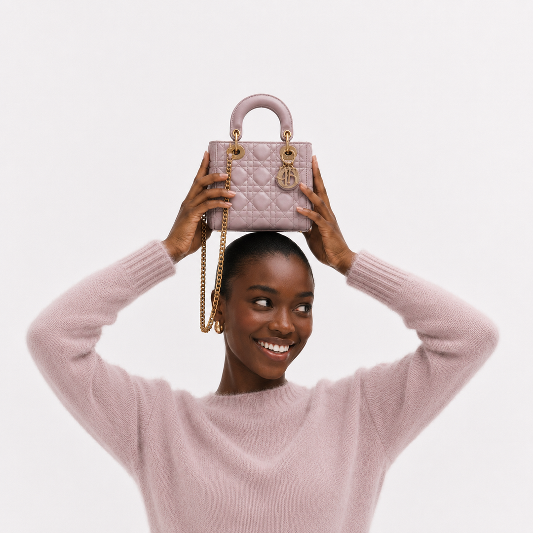 A woman in a light pink knit sweater holds a matching light pink quilted top-handle handbag above her head against a plain light gray studio background.