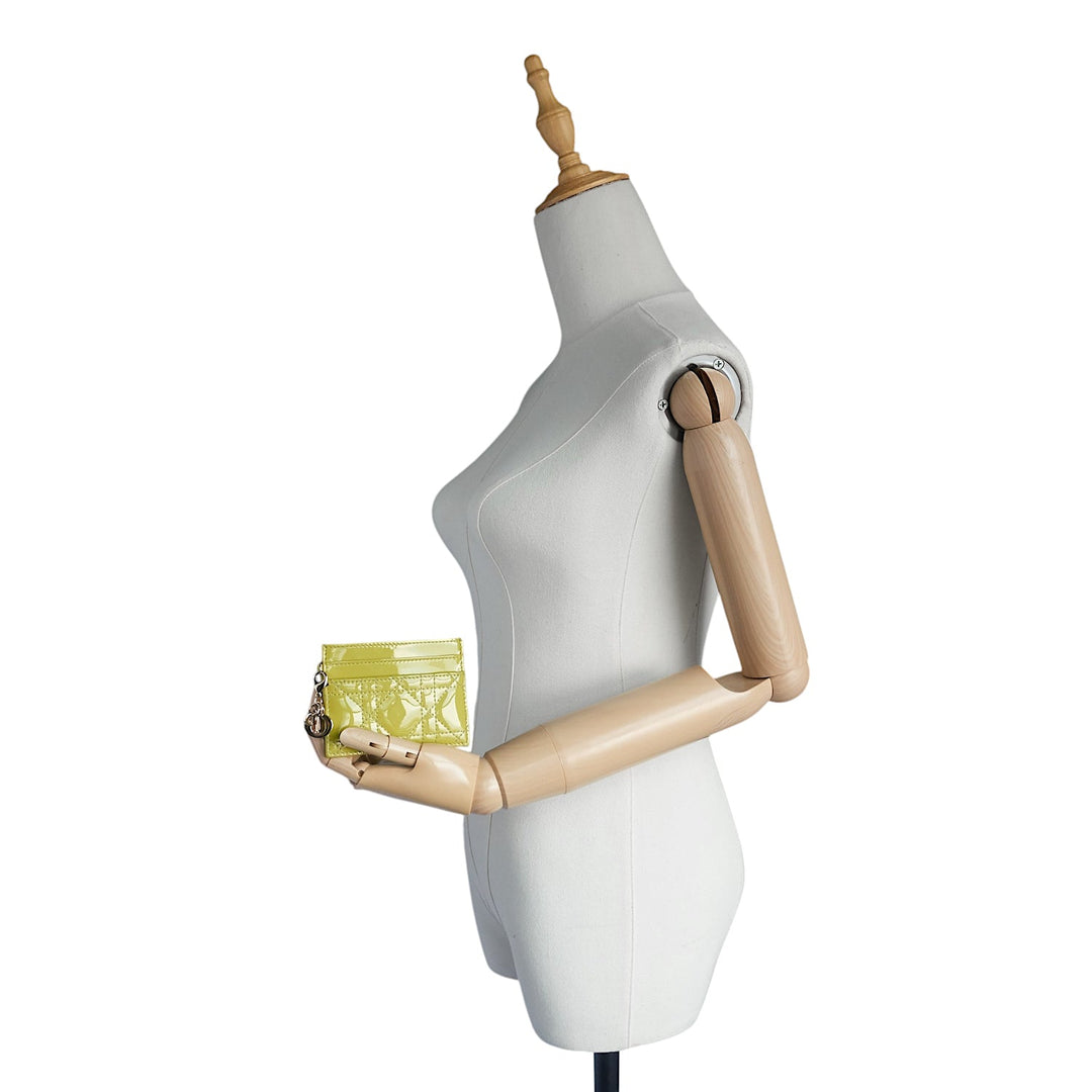 A white dress form mannequin with articulated wooden arms holding a small lime green patterned clutch bag, shown against a plain white background.