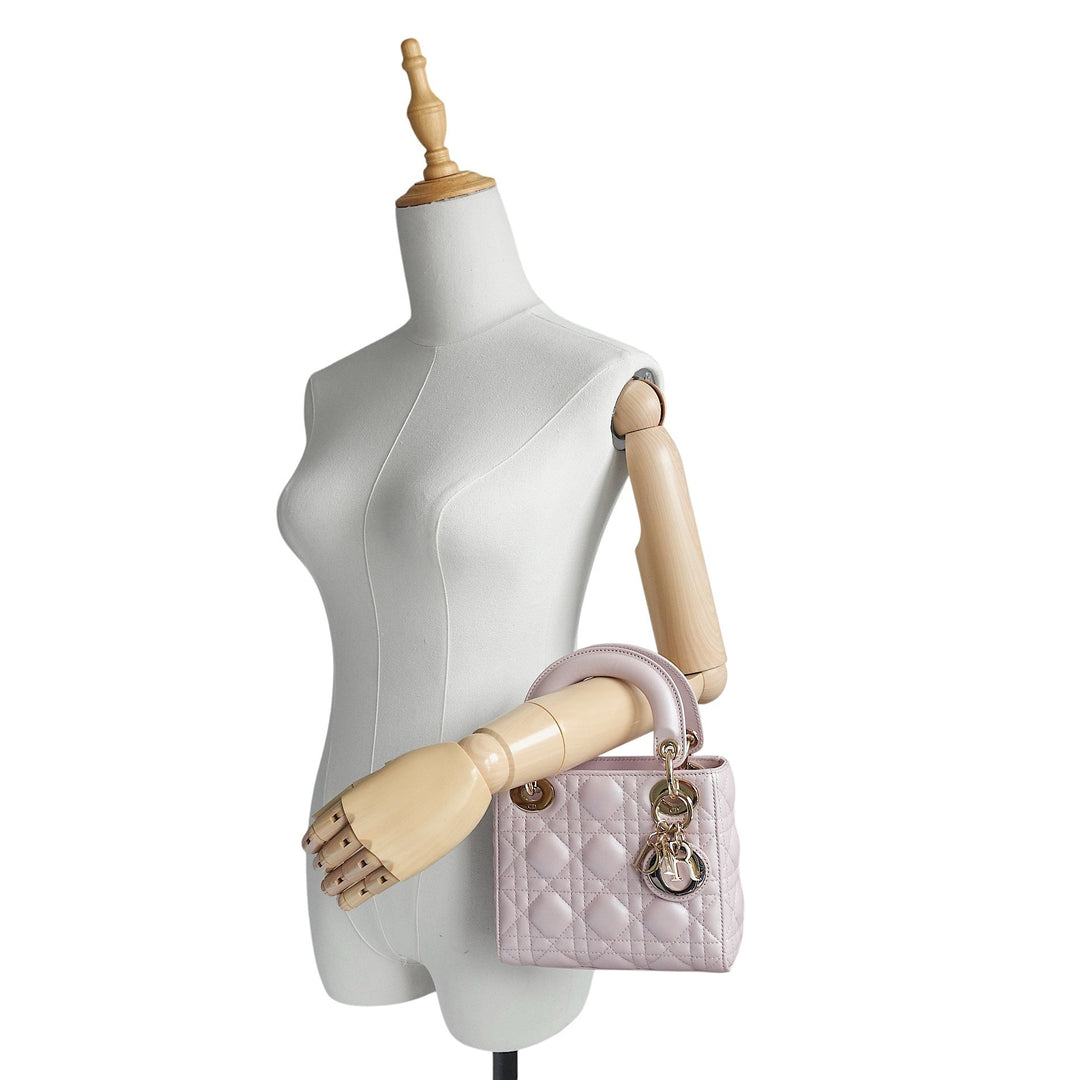 A light pink quilted leather handbag with gold-tone hardware, displayed on a white female mannequin torso with wooden arms against a white background.