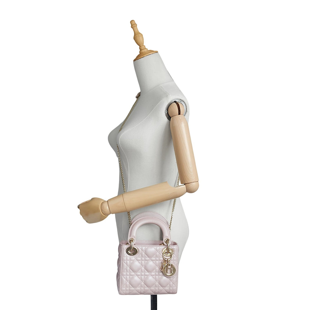 A light pink quilted Christian Dior Lady Dior handbag with gold-tone hardware, displayed on a white female mannequin torso with wooden arms against a white background.