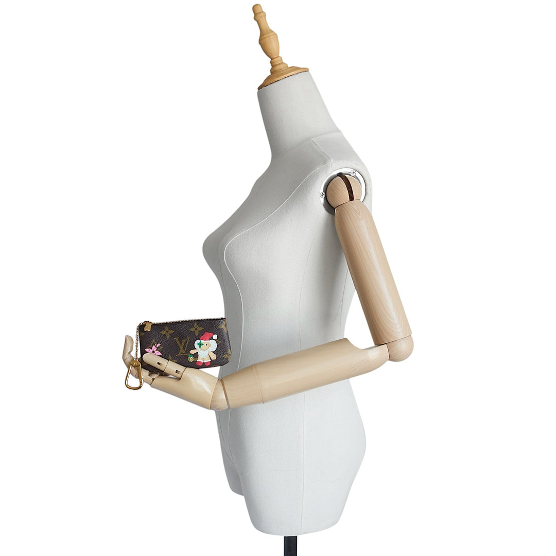 A white torso mannequin with wooden arms and neck is shown against a white background, holding a small dark monogram clutch bag with a cartoon character print.