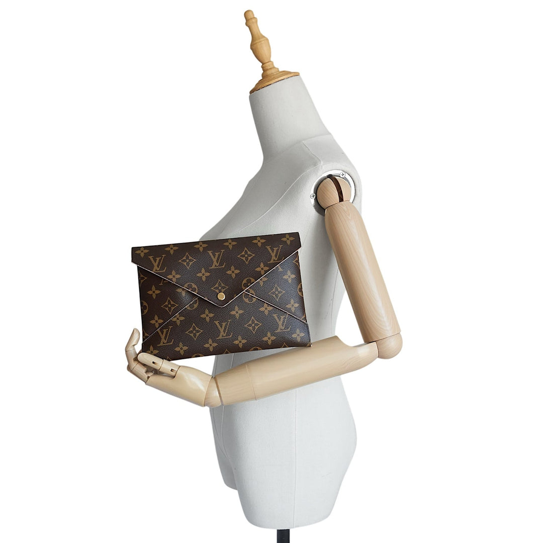 A Louis Vuitton monogram envelope clutch bag in brown coated canvas, displayed on a white mannequin torso with wooden arms against a plain white background.