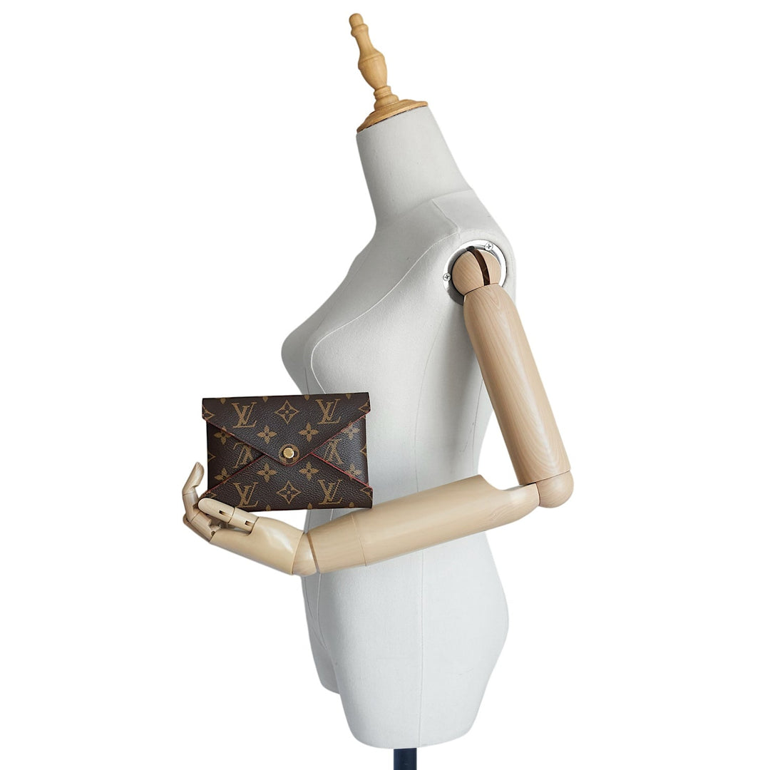 A Louis Vuitton monogram envelope clutch bag in dark brown coated canvas, held by a white female wooden mannequin against a plain white background.