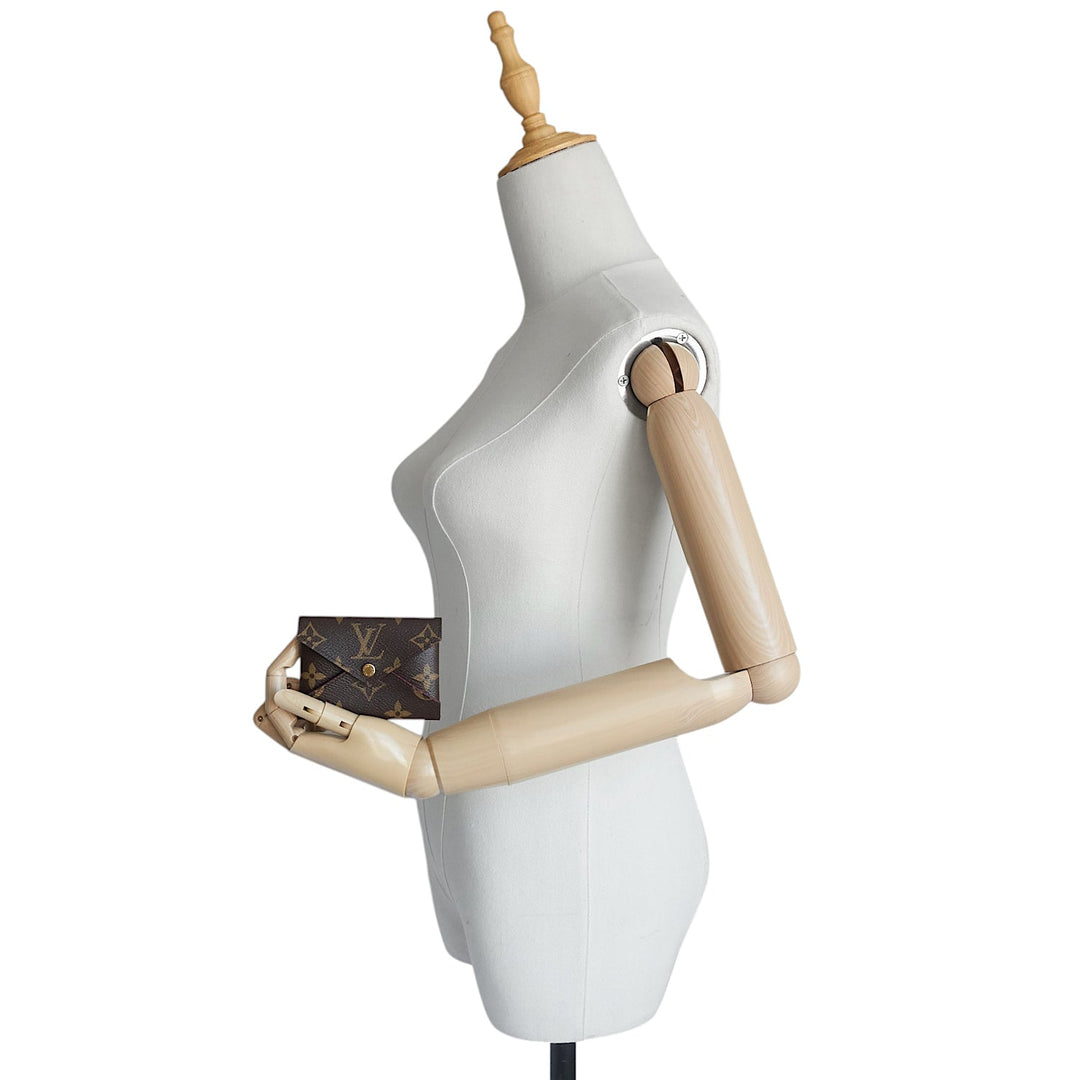 A Louis Vuitton monogram canvas clutch bag held by a white female dress form mannequin with wooden arms against a white background.
